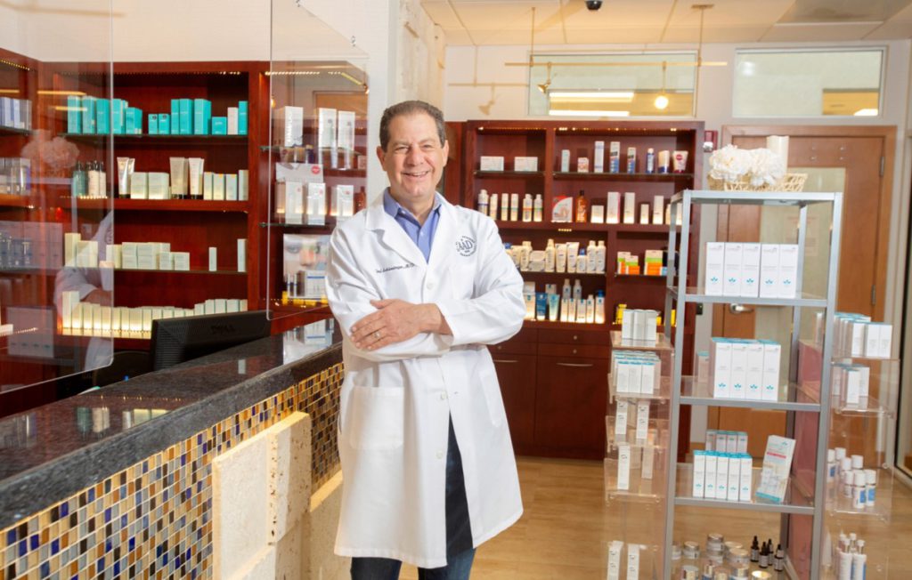 Dr. Schlessinger Smiling with his arm crossed in the LovelySkin Med Spa surrounded by skincare products