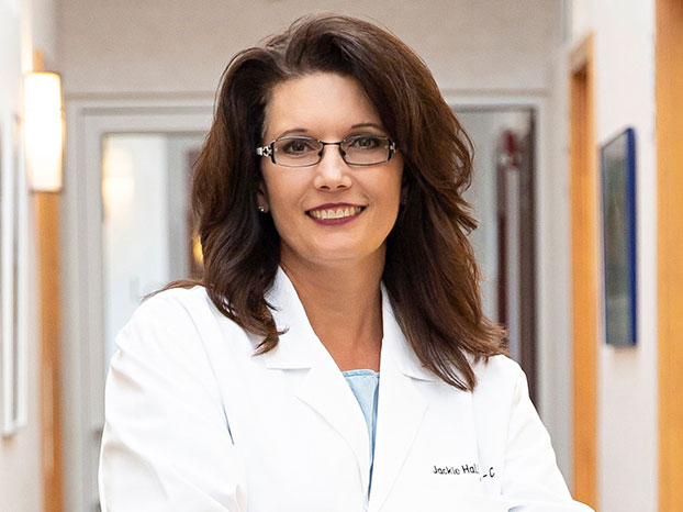 Profile of Physician Assistant Jakie Hall in lab coat standing in a hallway inside Schlessinger MD office