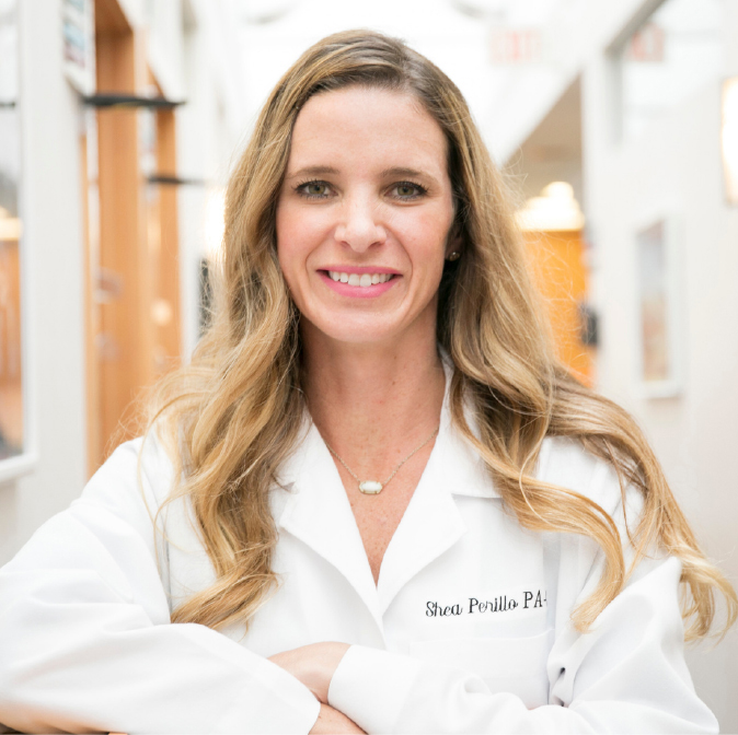 Profile of Physician Assistant Shea Perillo in lab coat standing in hallway inside Schlessinger MD office