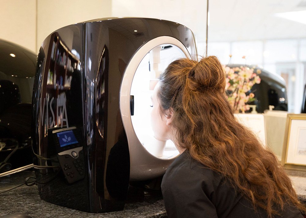 Long haired brunette woman sticking face inside of Visia Skin Analysis Device